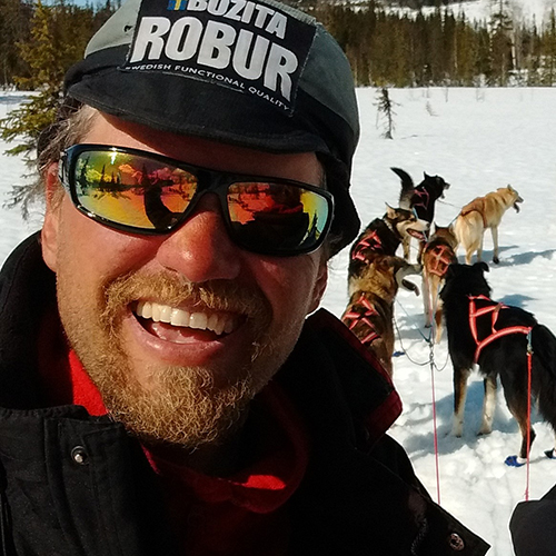 a man smiling for a picture with dogs in the snow